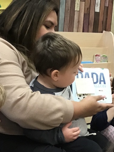 educator sitting with child showing book from home to other children 