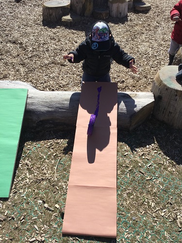 Preschool child rolling wheel down ramp with paint 