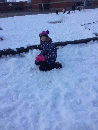 School-age girl rolling snow boulder 