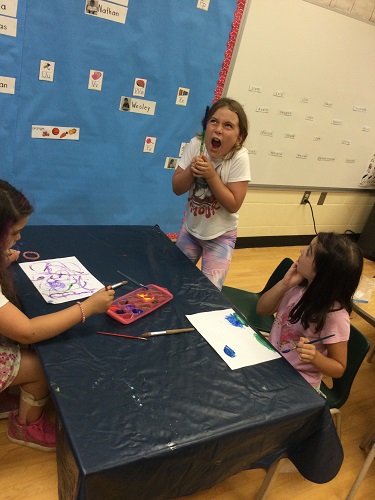 2 school-age girls painting while another school-age girls holds up her wand