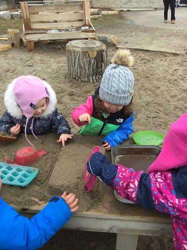 Group of toddlers making mud cakes in sandbox