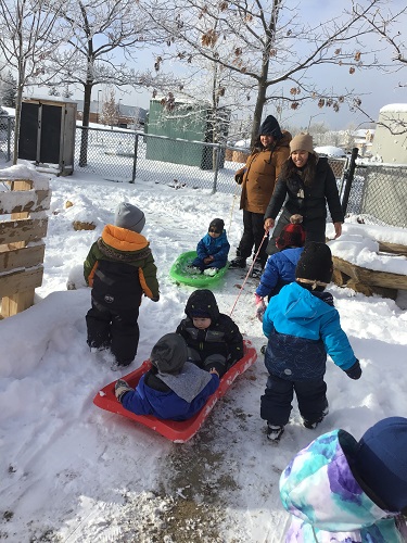 Educator pulling sled while toddlers follow