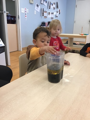 A toddler is dropping a Mentos candy into a container containing oil, coke, and food colouring.