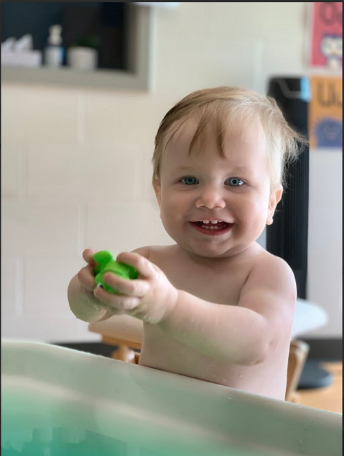 A child smiling as they explore with water and a toy frog.