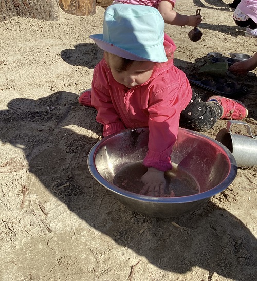 A child dipping her hand in a water and sand mixture