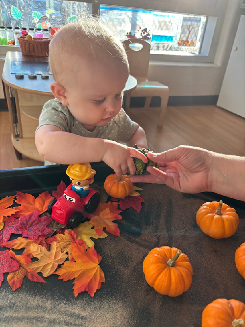 A child taking a gourd from an educator's hand.