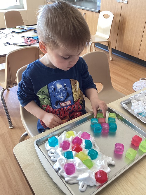 A child exploring with shaving foam and loose parts.