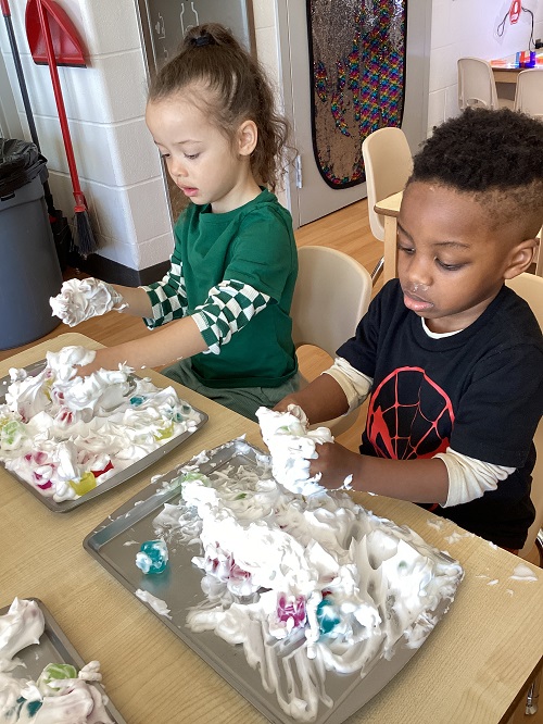 Two children exploring with shave foam and loose parts.