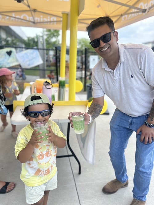 A child standing with an adult as they enjoy their lemonade.