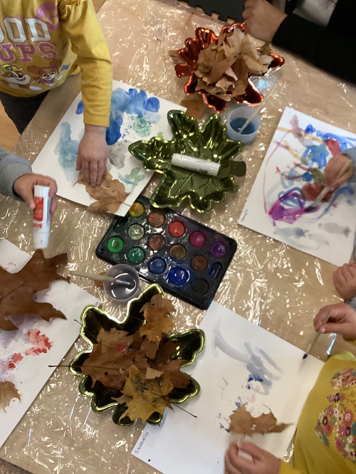 Asmall group of children exploring with paint, glue, paint and natural fall loose parts.