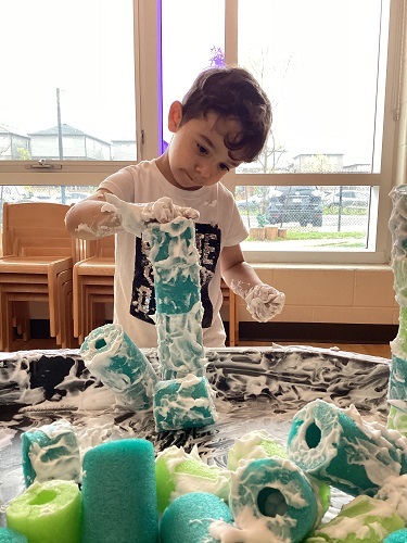 A child building a tower with the shaving cream covered pool noodles.