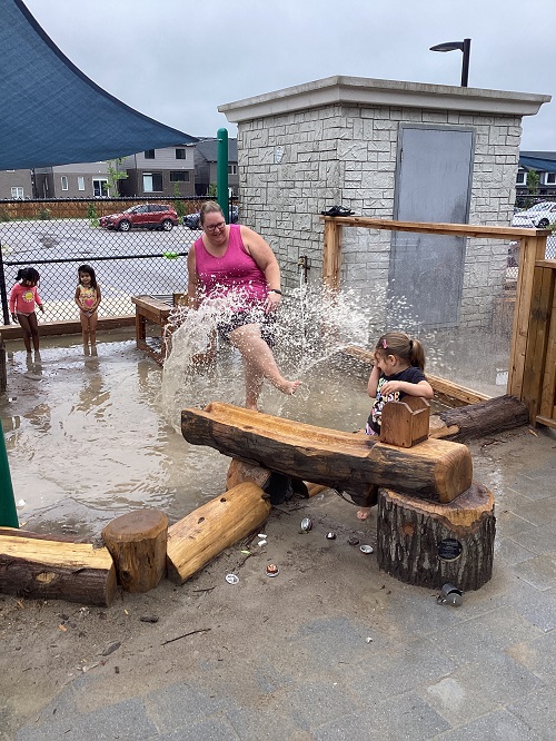 A child and educator exploring and splashing in the water on the playground.