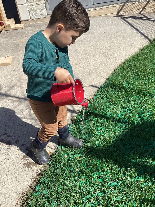 A child watering the grass with a watering can