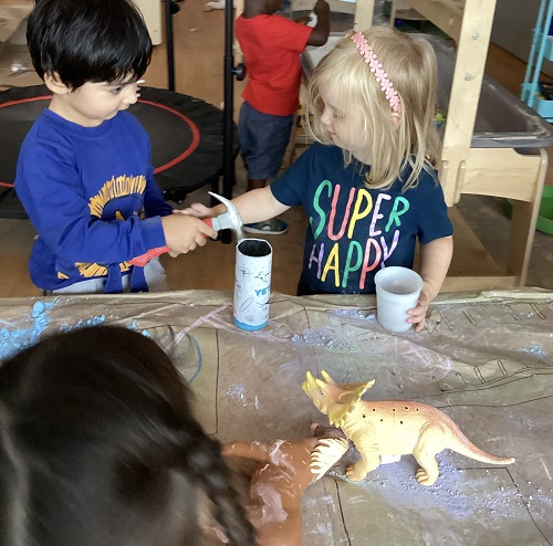 A child encouraging their peer to use a hammer.