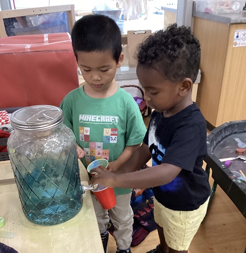 Two children using a water dispenser together.