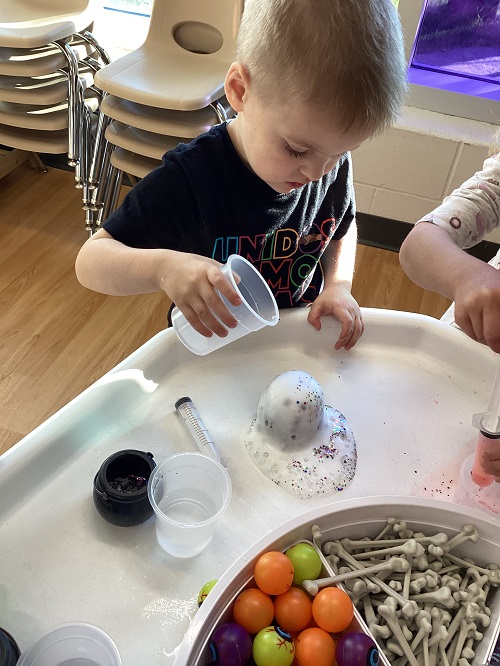 A child pouring vinegar into the baking soda filled cauldron.