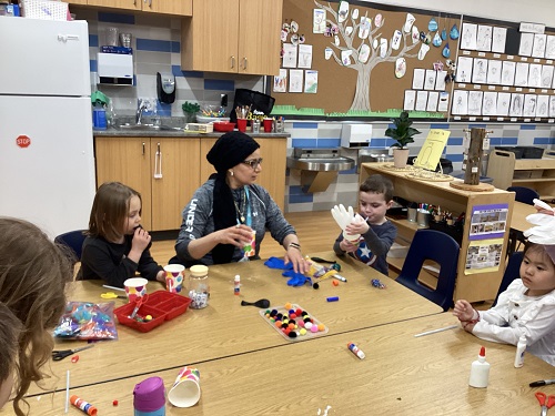 A group of children sitting at a table with an Educator working with art materials.