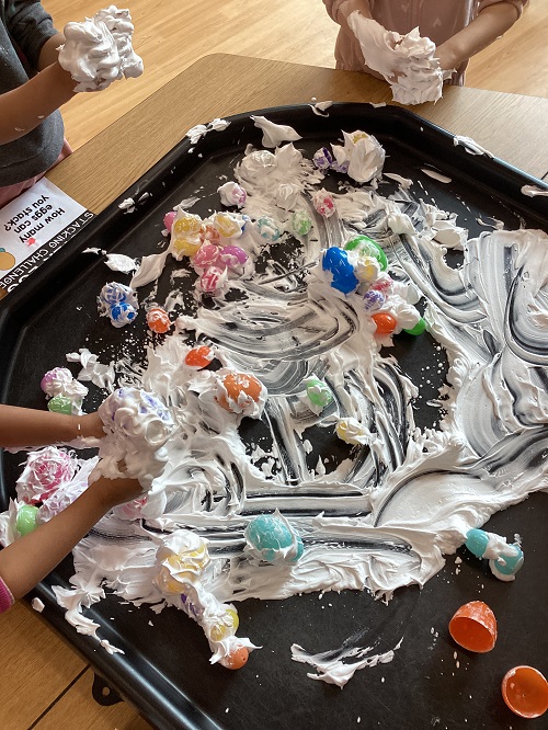 A tuff tray filled with shaving foam and colourful treasures.