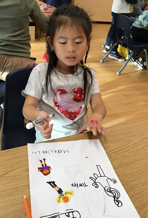 A child sitting in front of a picture they drew.