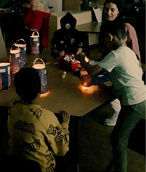 Children sitting at a table with an educator with lanterns they created.