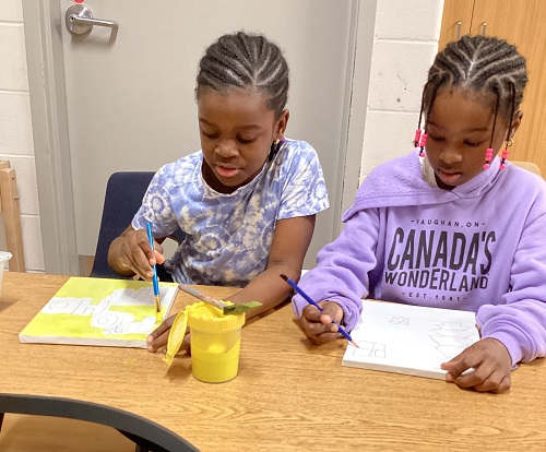 Two children sitting at a table, painting canvases.