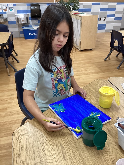 A child sitting at a table painting a canvas.