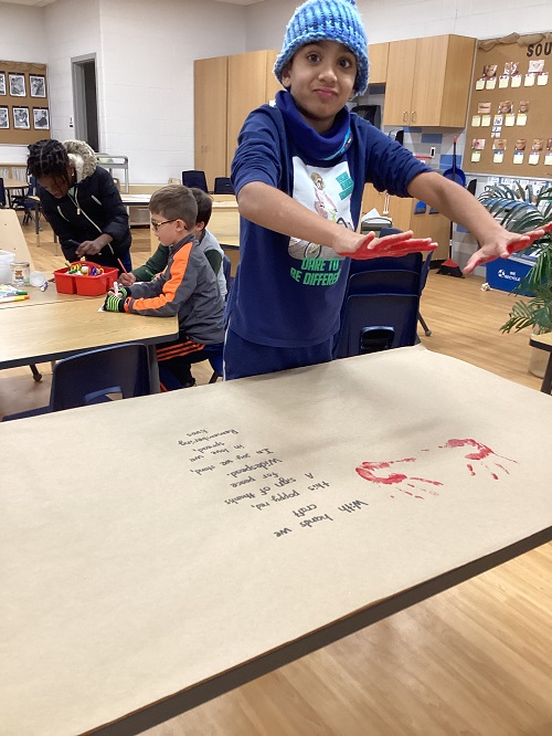 A child with red paint-covered hands had just applied their hand prints to their group creation.