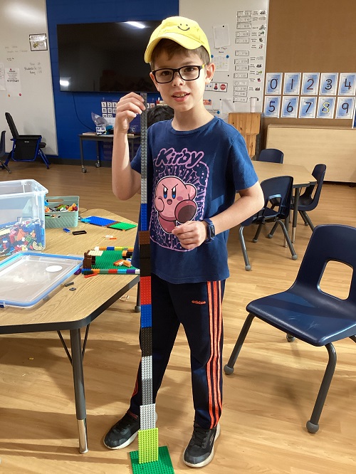 A child standing next to their structure they built with lego.