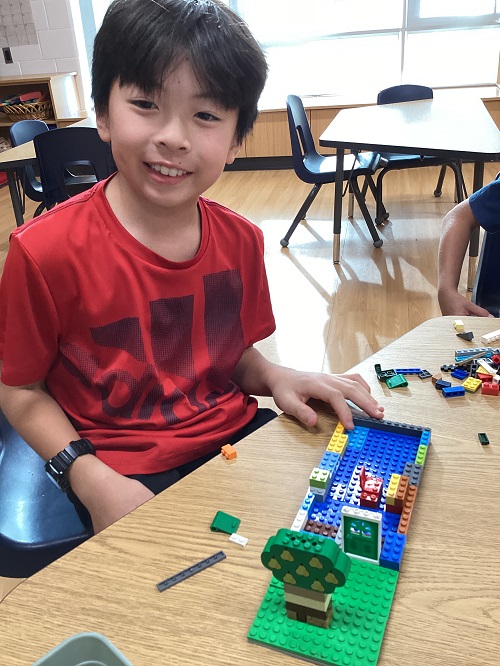 A child smiling while showing the lego structure they built.