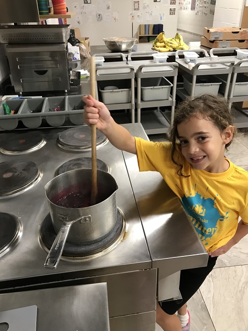 A child stirring blueberry jam they are cooking on the stove.