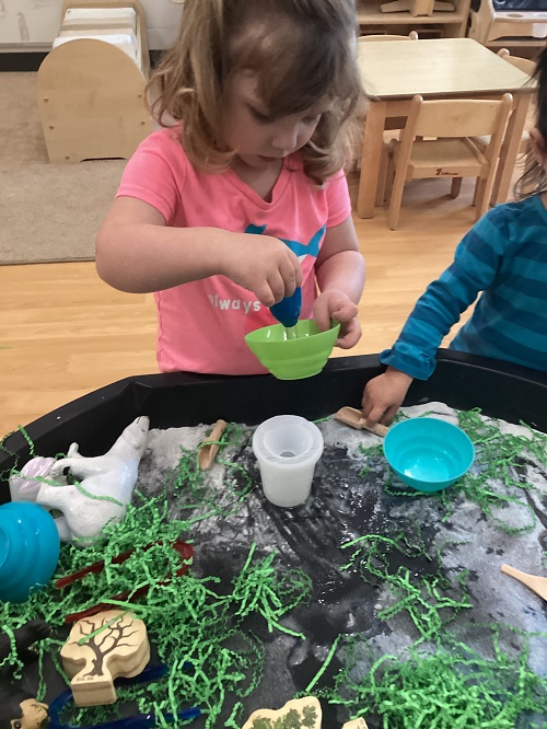 A child exploring with water in the animal habitat tuff-tray.