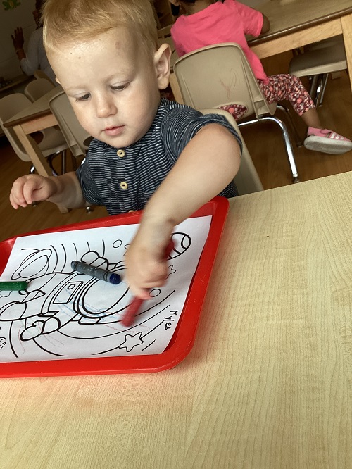 A child using crayons to colour their picture.
