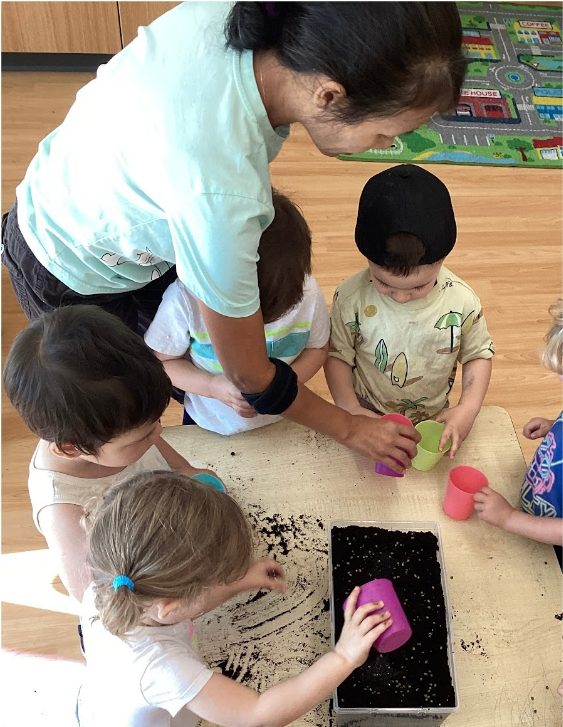 An educator handing seeds to children to plant in the soil-filled bin.