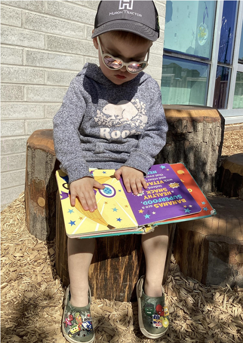 A child sitting on a stump while reading a book