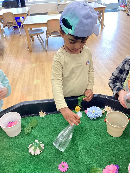 A toddler child using a spray bottle to water artificial flowers