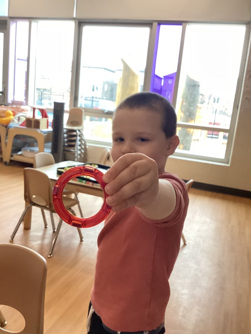 A preschool child holding a magnet tile shape