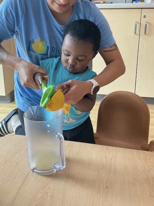 educator helping little girl squeeze the lemon