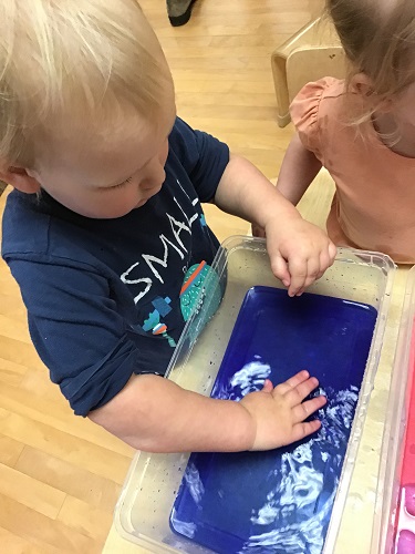 Toddler child putting hand on top of blue water in an open bin