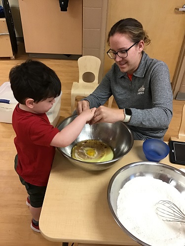 Child and educator cracking eggs into a bowl