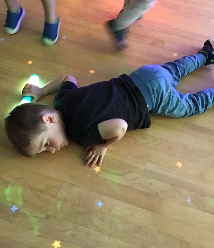 A child laying on the floor to look at lights reflecting on the floor