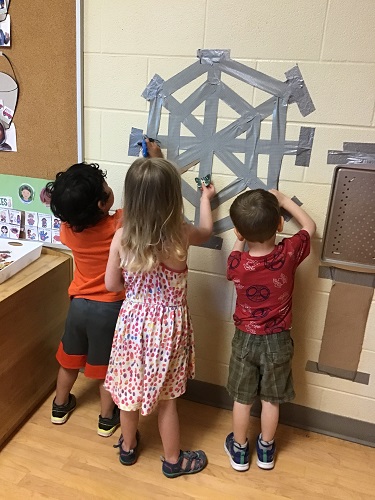 Children removing plastic bugs from a duct tape spider web