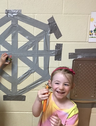 A child removing plastic bugs from a duct tape spider web