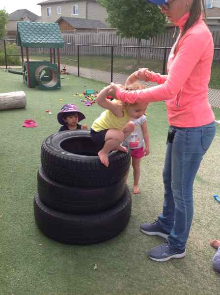 educator helping child jump off a stack of tires