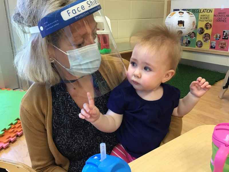 masked educator holding an infant sitting at a table
