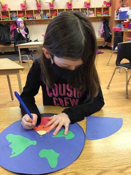 girl writing contanent names on a globe drawing