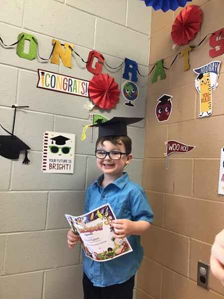happy preschool graduate holding certficate with graduation hat