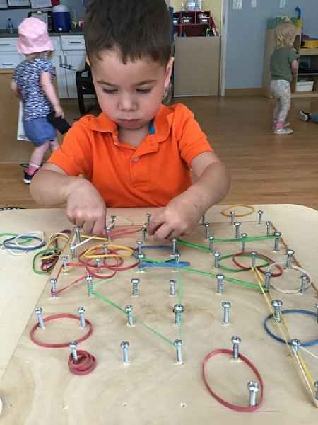 boy putting elastics around nails on a board