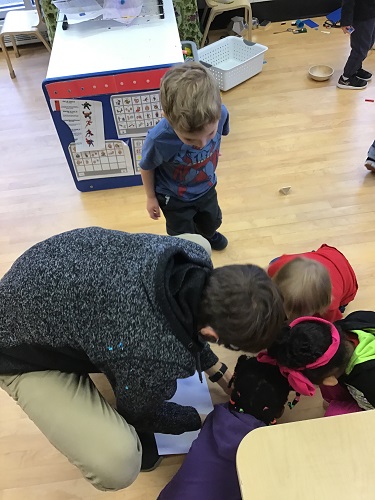 An educator and a group of children looking on the floor at a spider