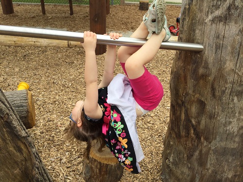  a child hanging off of the monkey bar on the natural playground