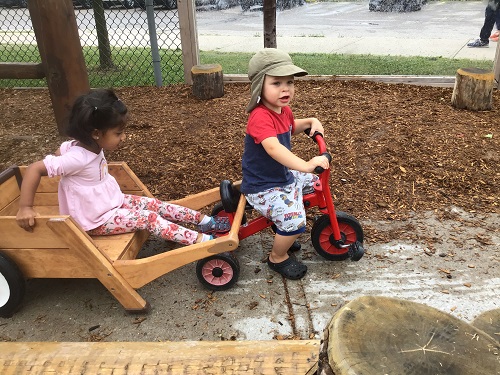 a child riding a bike, pulling another child in a wagon